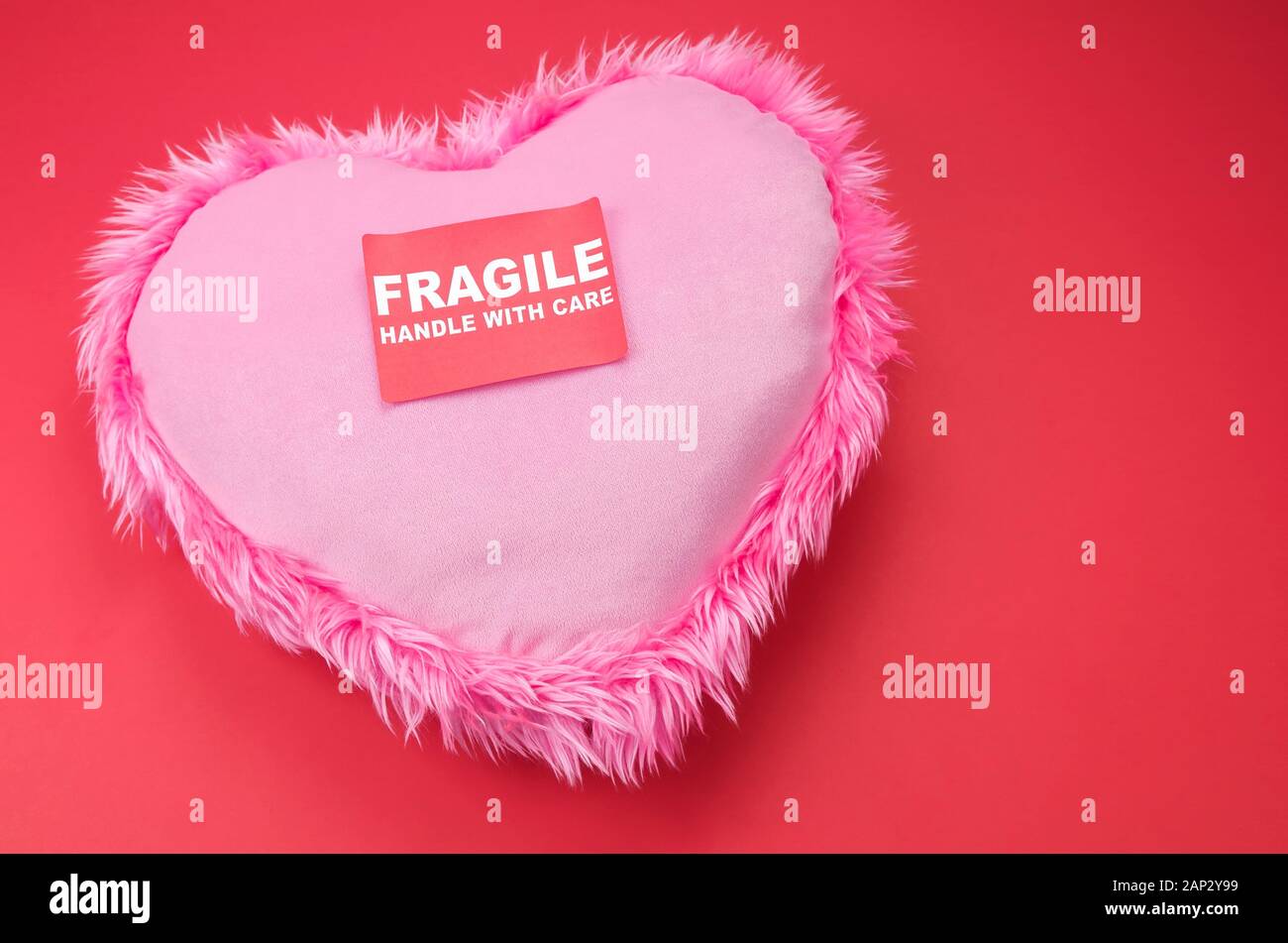 Pink heart with furry trim sitting on a bright red background with a Fragile Handle With Care Sticker Stock Photo