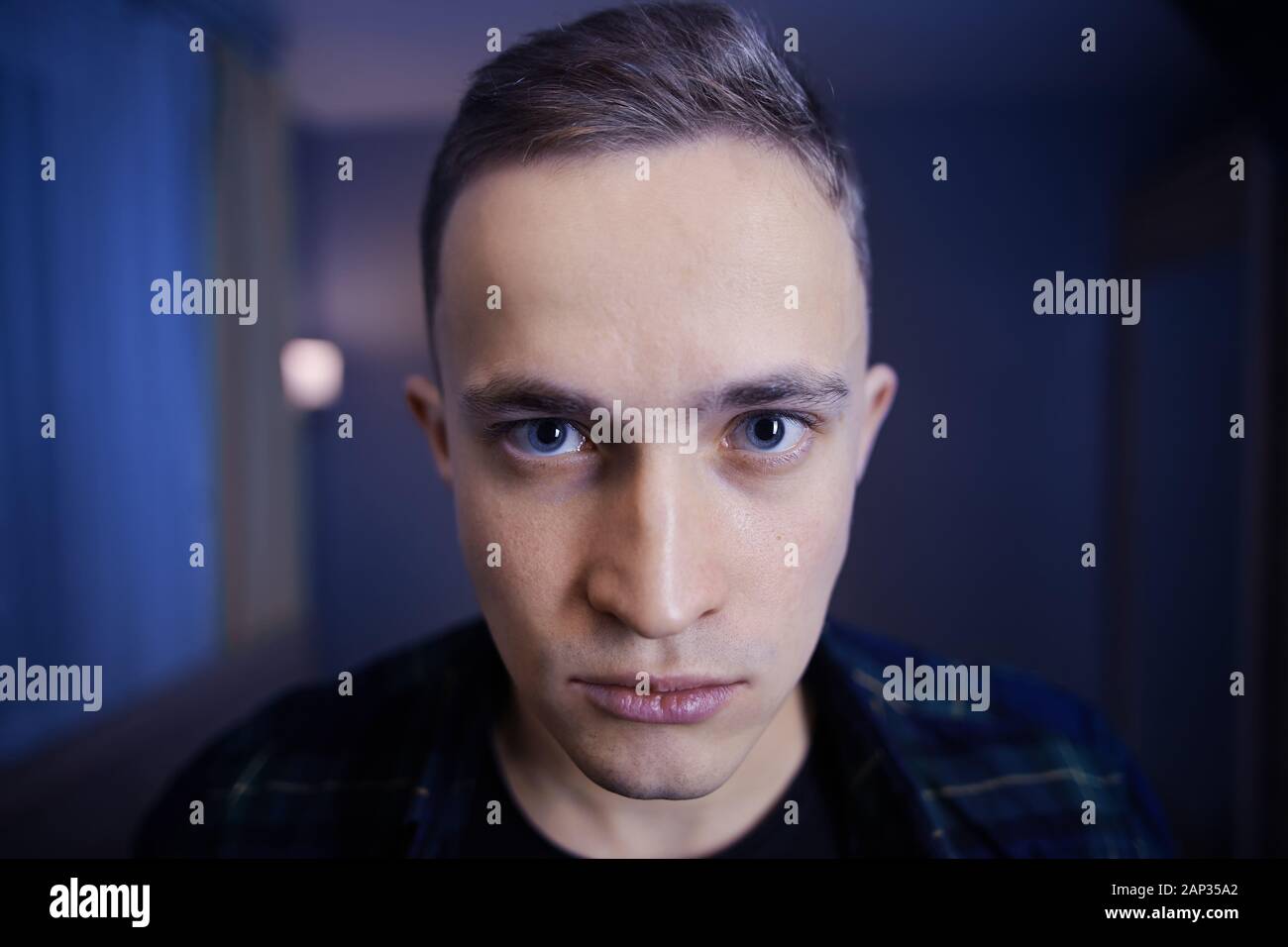 A depressed look on the face of a young Caucasian man with gray eyes and a short haircut. Paranoid white male in a dark blue room. The guy is 22 years Stock Photo