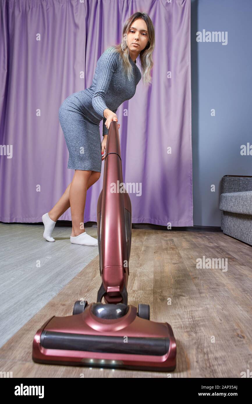 https://c8.alamy.com/comp/2AP35AJ/a-cleaning-lady-is-vacuuming-the-floor-with-a-vertical-vacuum-cleaner-or-an-electric-broom-a-slender-young-woman-in-a-slinky-dress-cleans-the-room-s-2AP35AJ.jpg