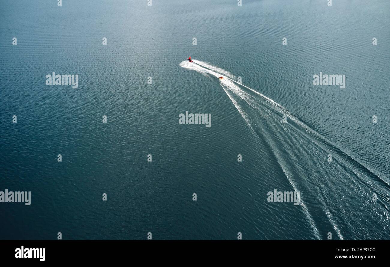 From above athlete water skiing on sea behind red motor boat among white foam and waves Stock Photo