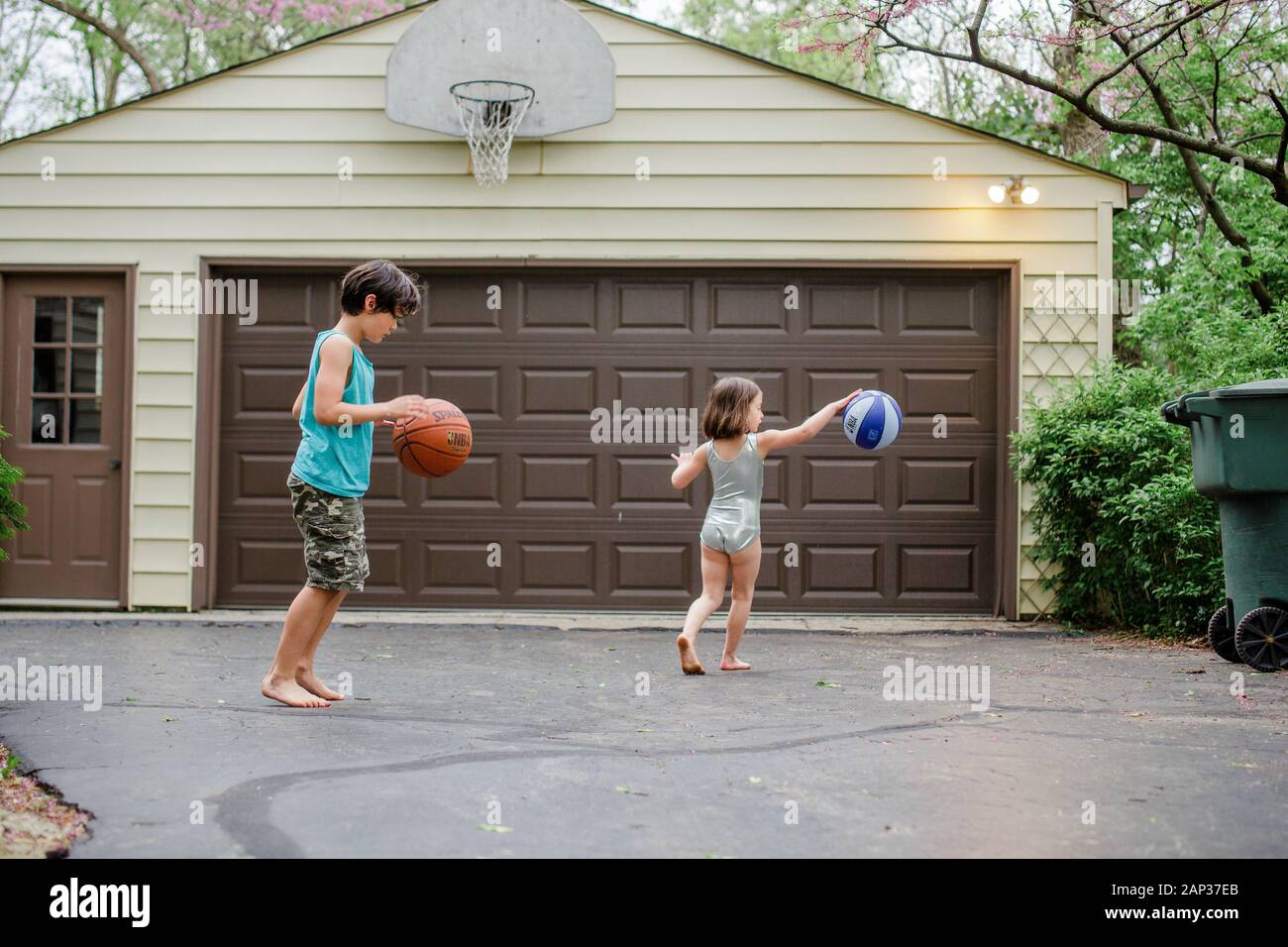 two little barefoot children dribble basketballs in a driveway Stock Photo
