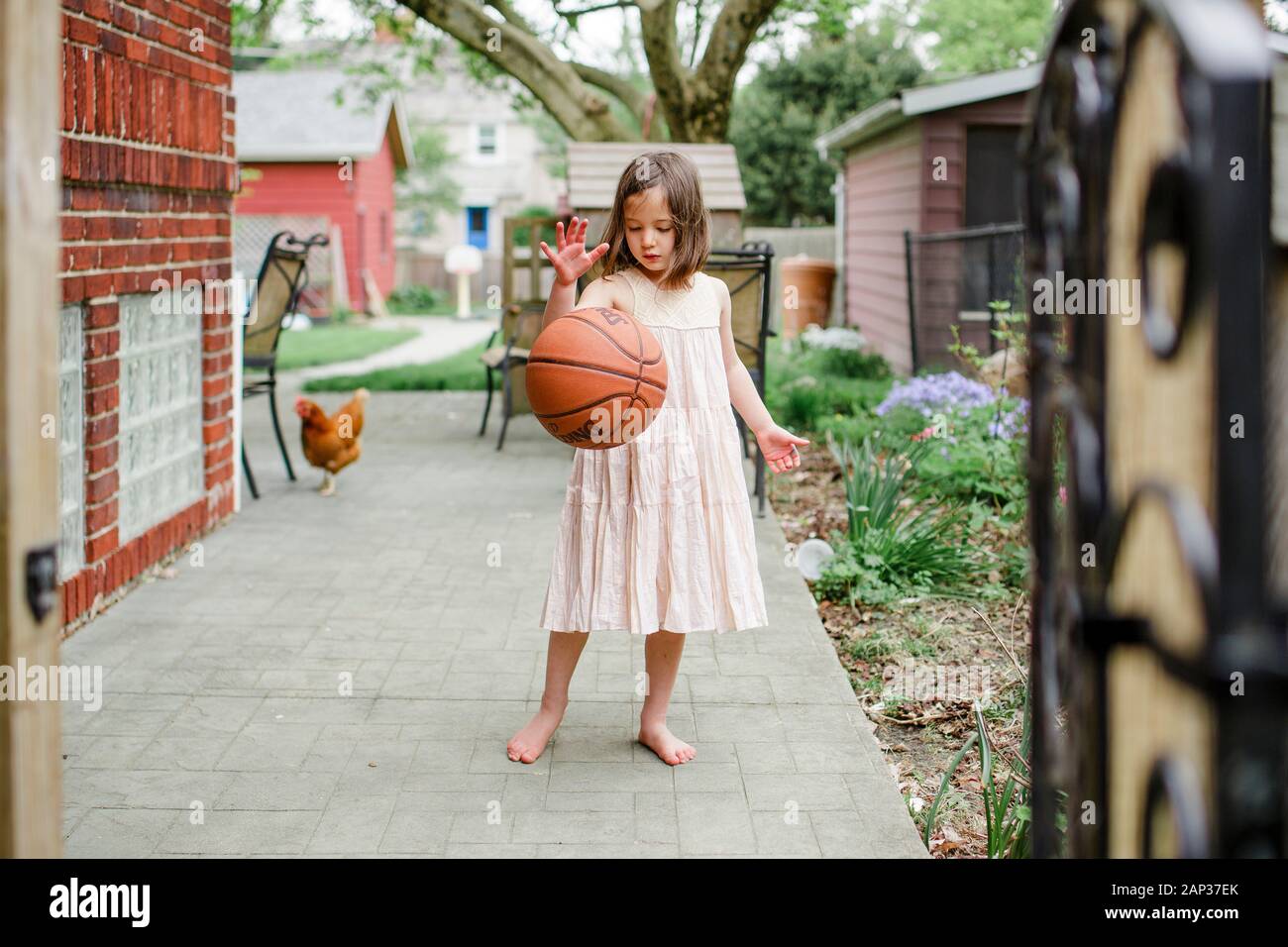 A girl stands with basketball mid-dribble with chicken behind her Stock Photo