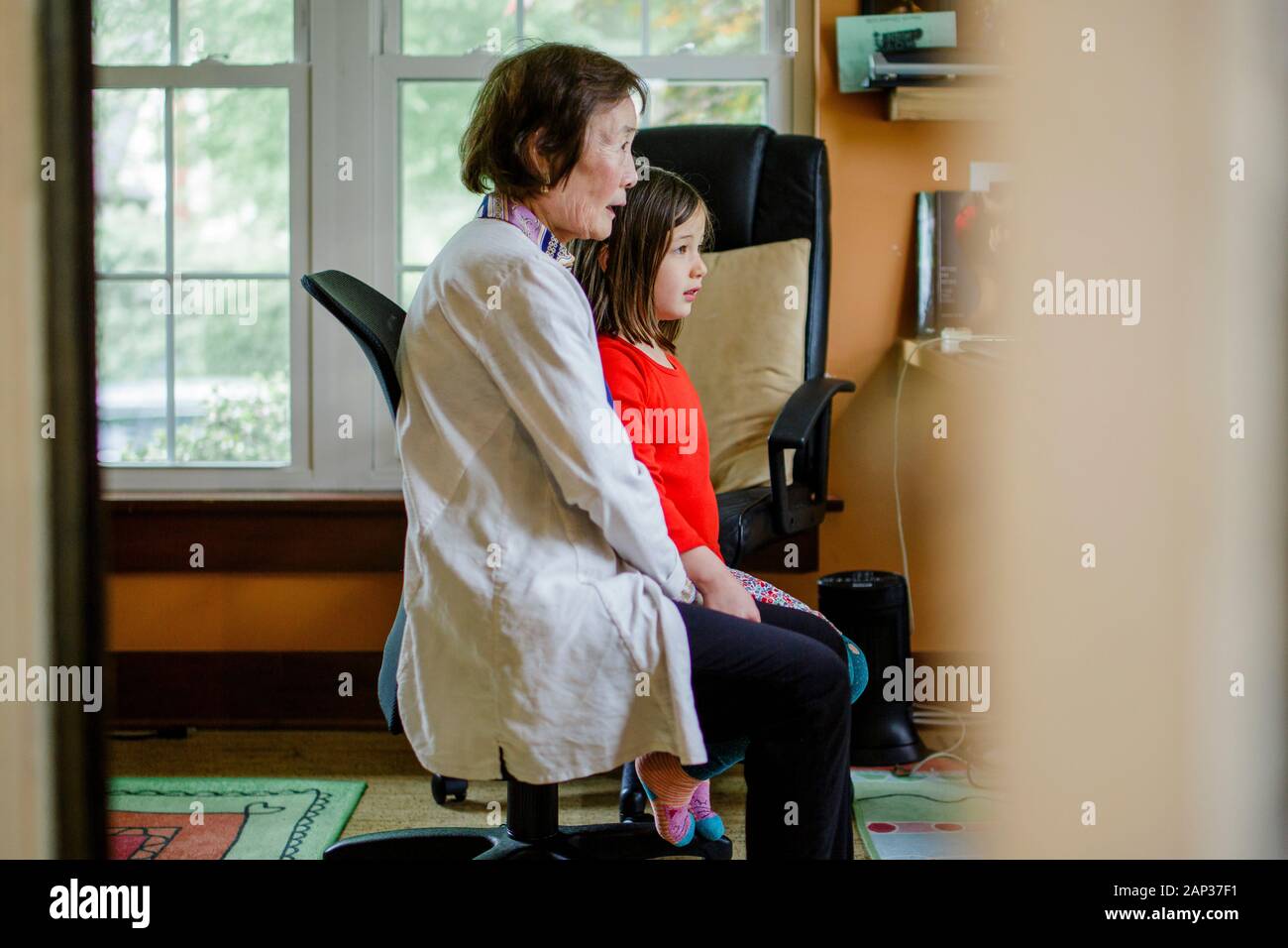 Side-view of grandmother and child sitting close together watching tv Stock Photo