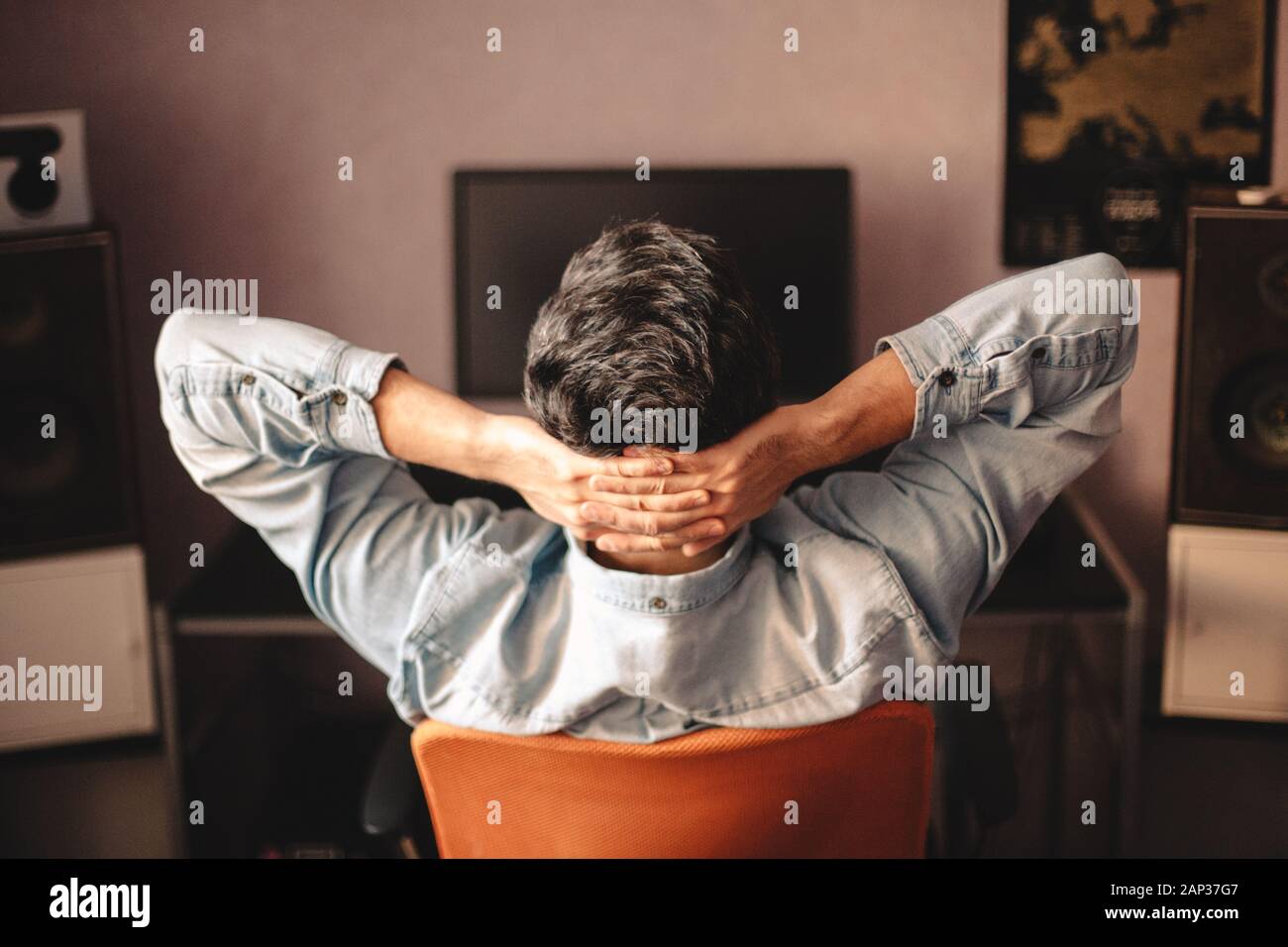 Man relaxing sitting on chair by computer with hands behind head Stock Photo