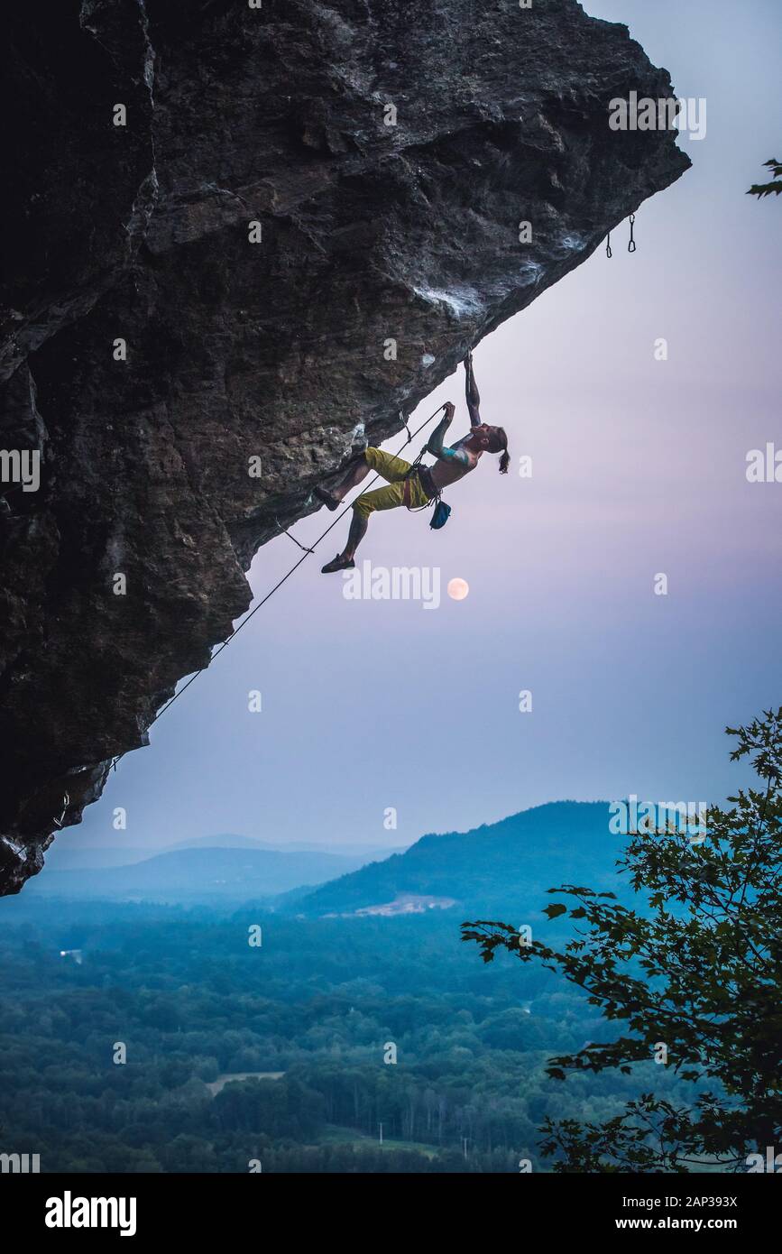 Man clipping quickdraw on overhanging sport climbing route with moon