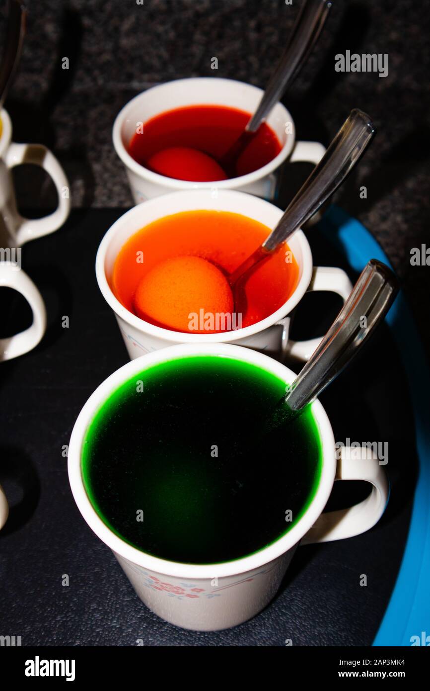 Coloring hard boiled Easter eggs in coffee cups, vertical Stock Photo