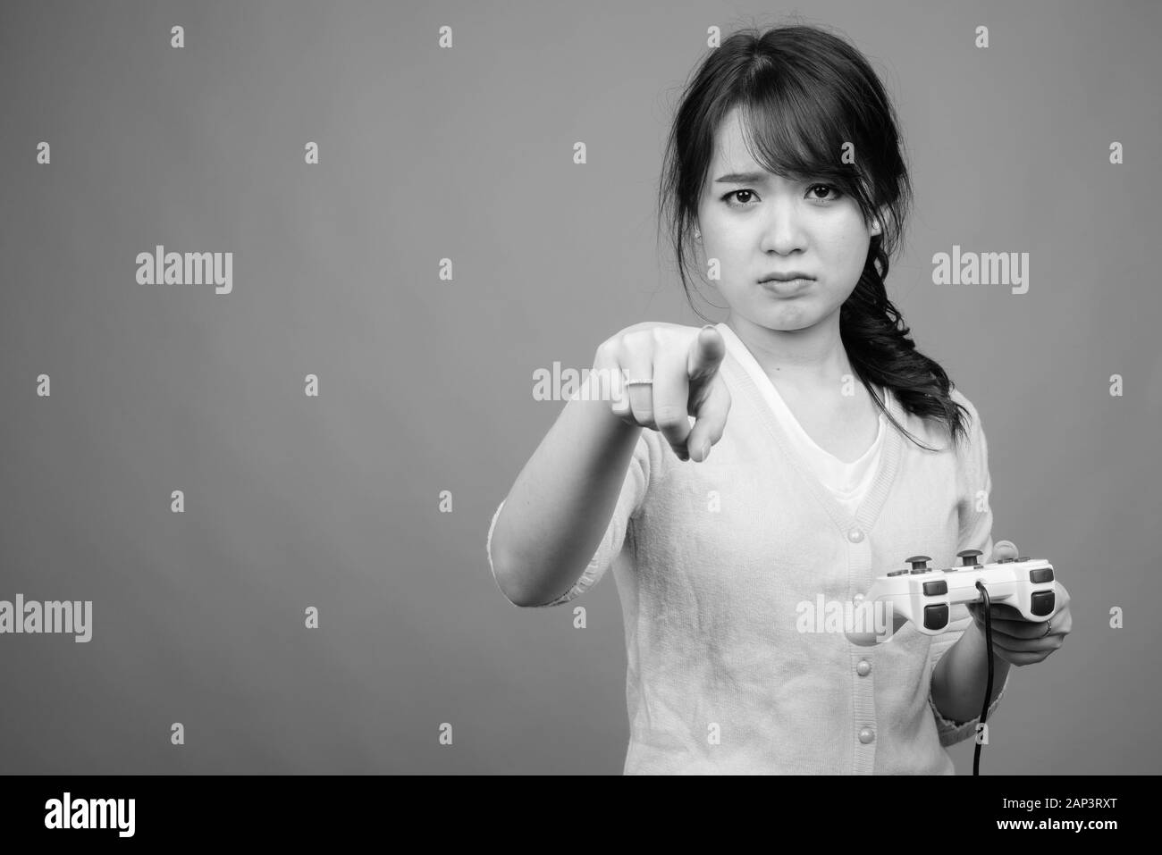 Young beautiful Asian woman playing games against gray background Stock Photo