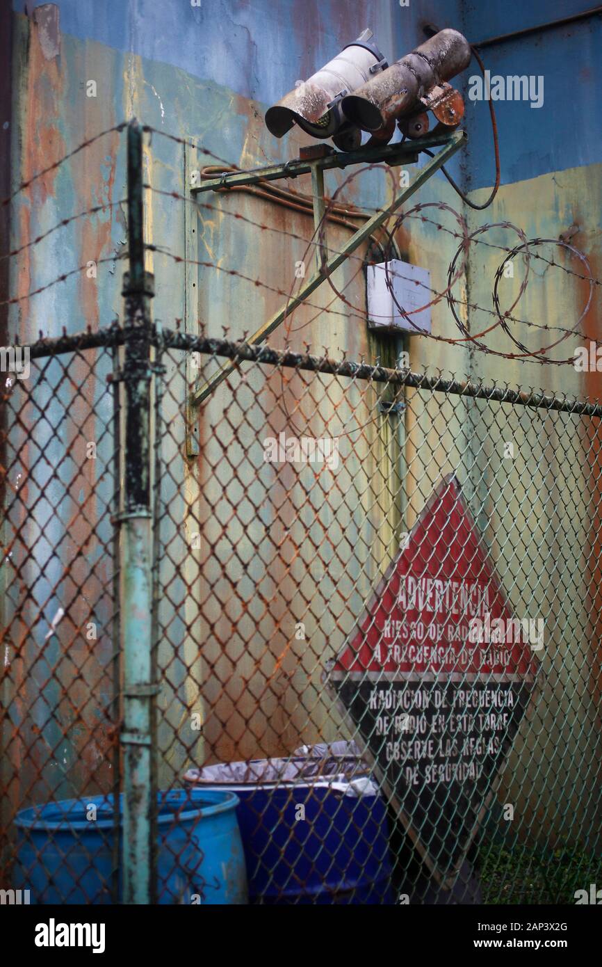 Surveillance cameras atop a chain link fence surrounding a rusty, aging building exterior. Stock Photo