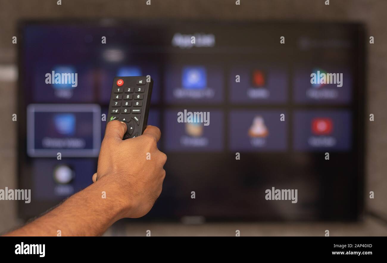 Maski, India 18,January 2020 - Hands holding remote control with different online subscription apps on TV screen in out of focus Stock Photo