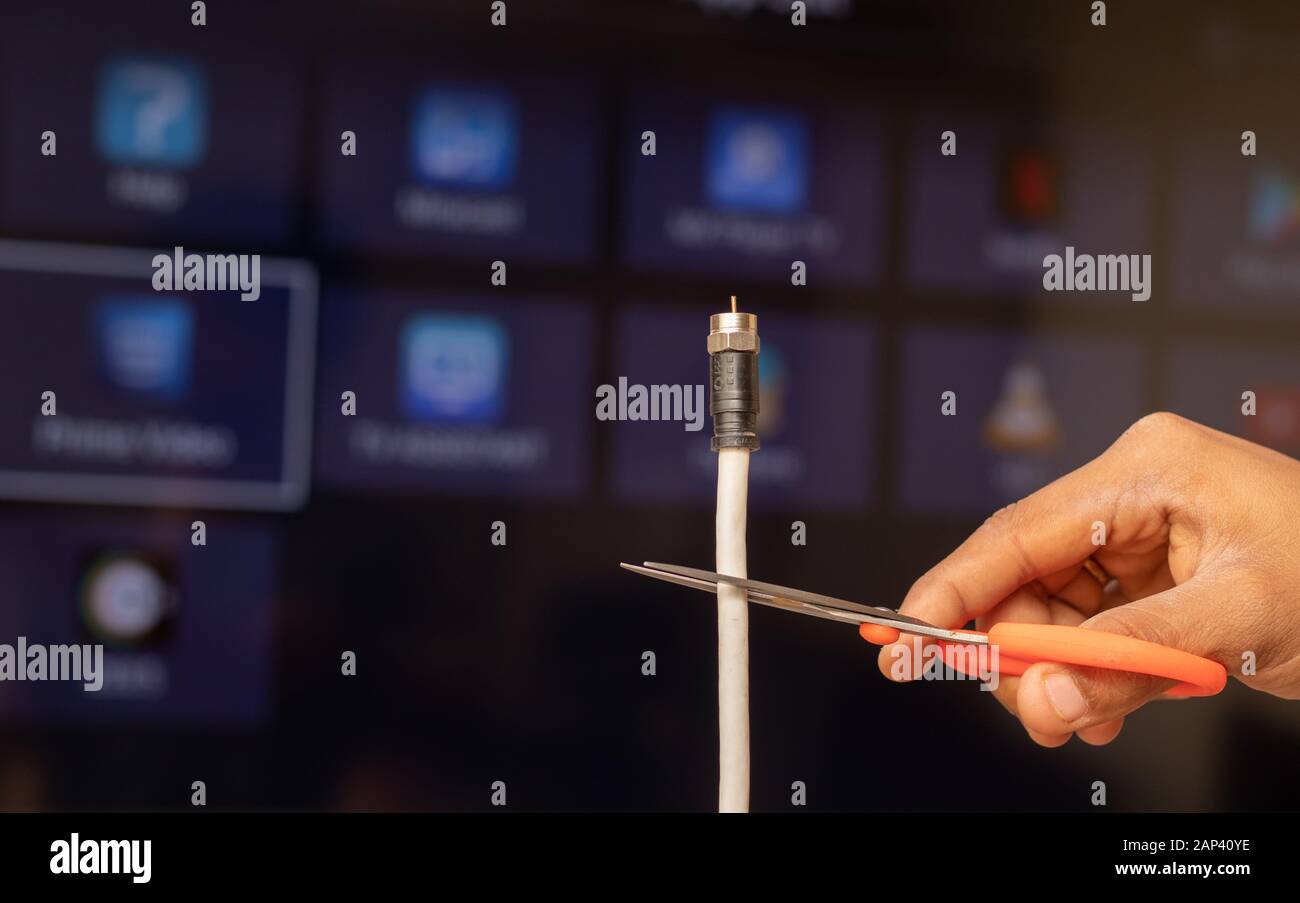 Maski, India 18,January 2020 - Hand cutting TV cord in from of the Smart TV showing different Streaming services in out of focus as a background Stock Photo