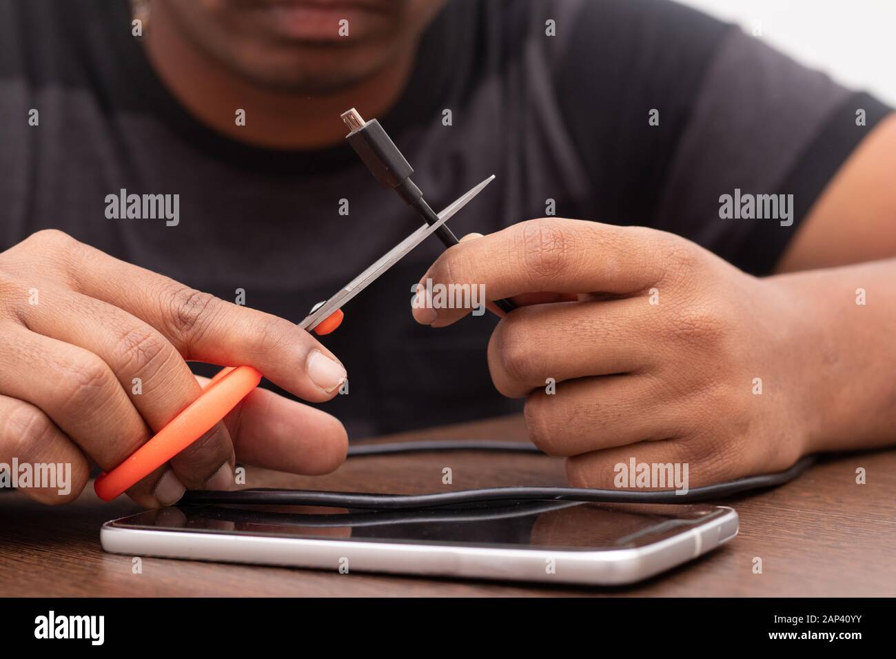 Hands cutting the Micro USB charging and data cable or cord with scissor. Stock Photo