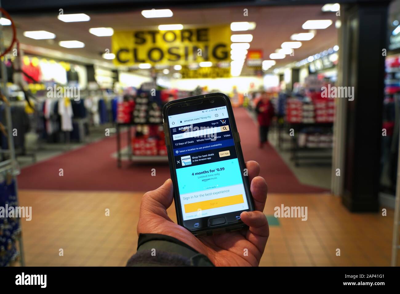 Storrs, CT USA. Dec 2019. Smartphone with giant online retailer Amazon homepage in hand of customer entering a store with permanently closing banner. Stock Photo