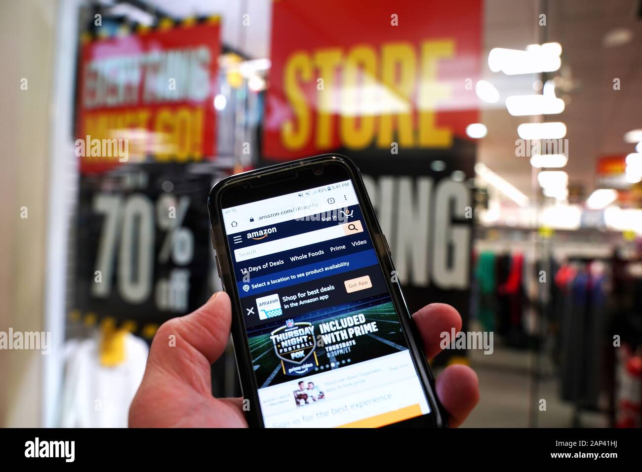 Storrs, CT USA. Dec 2019. Smartphone with online retailer Amazon homepage in hand of customer entering a store with permanently closing sign. Stock Photo
