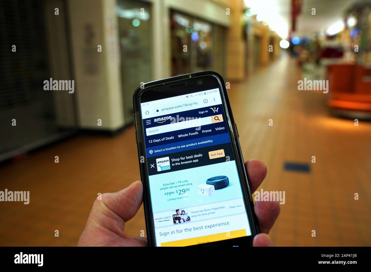 Storrs, CT USA. Dec 2019. Smartphone with giant online retailer Amazon homepage in hand of a visitor walking in an empty mall. Stock Photo