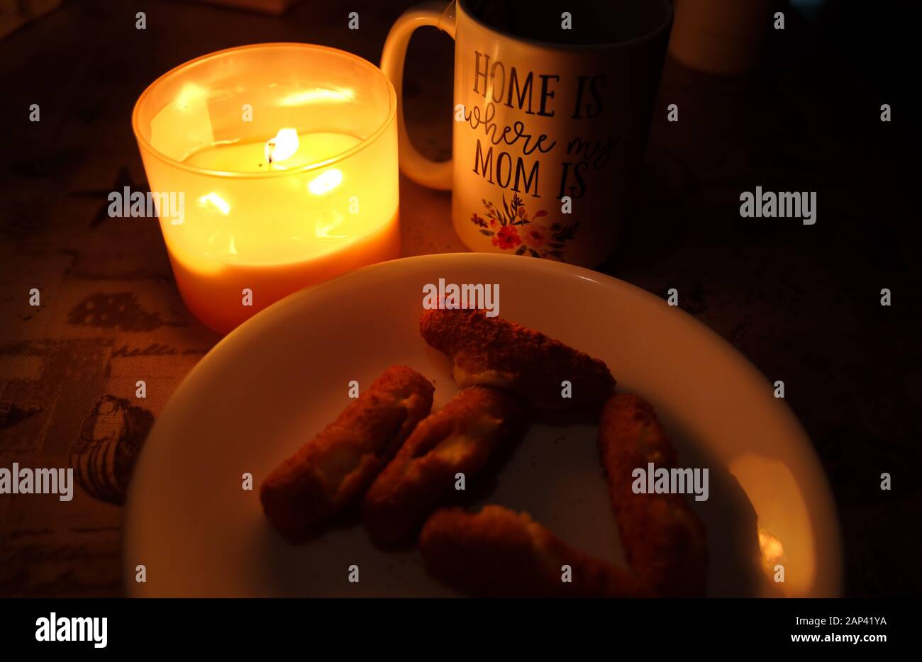 Cup with message of motherly love and home under candle light, and a plate with a treat mozzarella sticks for mom. Stock Photo