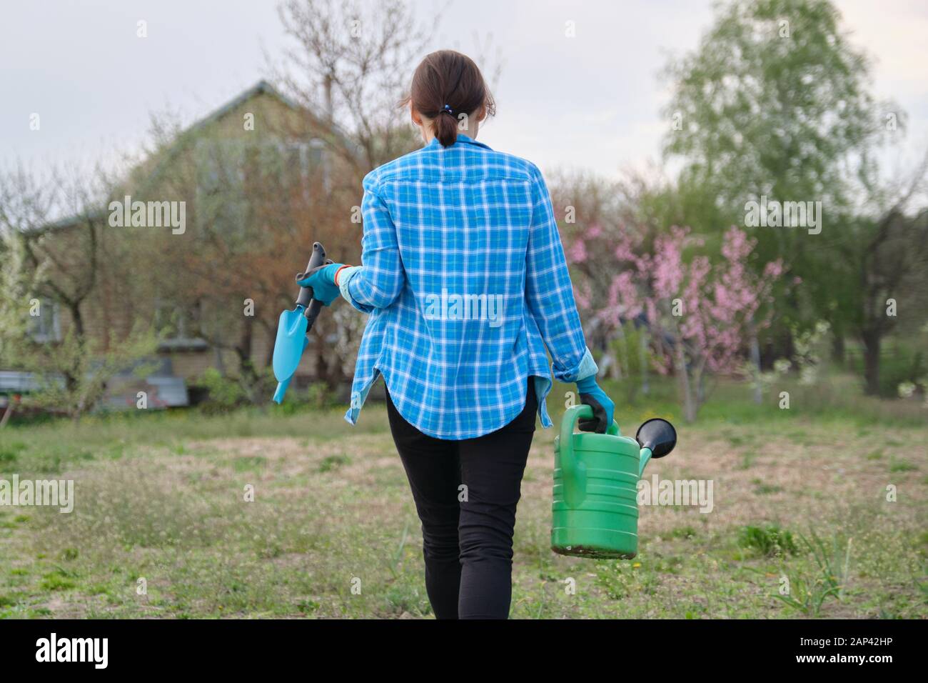 Female gardener holding watering can and garden tools Stock Photo - Alamy