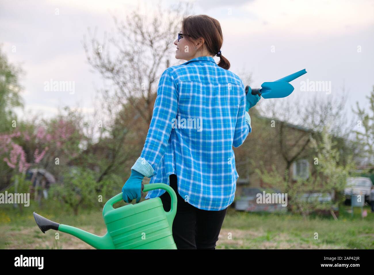 Female gardener holding watering can and garden tools Stock Photo - Alamy