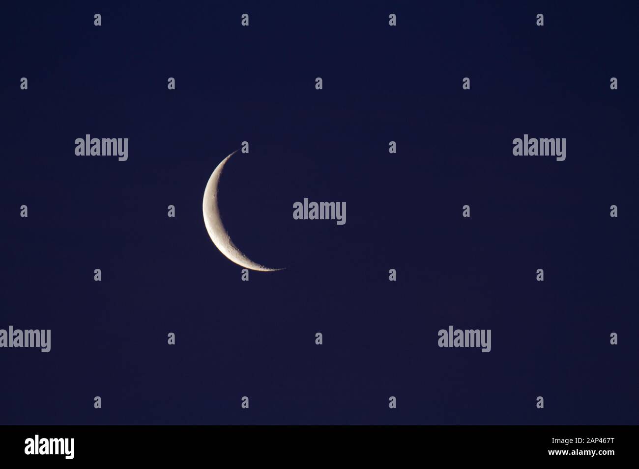 Waning crescent moon in dark blue sky Stock Photo