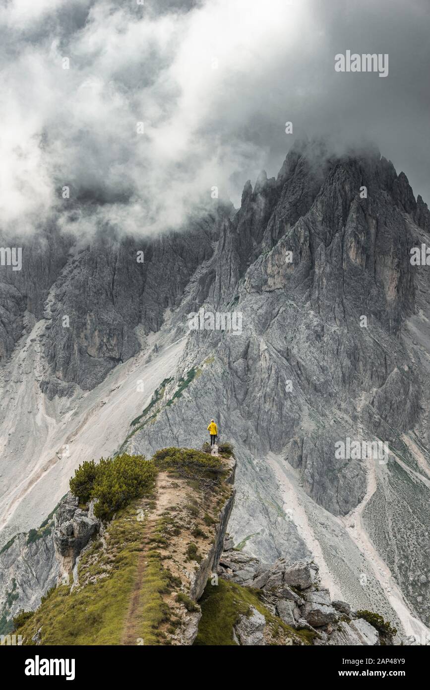 Woman in yellow jacket standing on a ridge, behind her mountain peaks and sharp rocky peaks, dramatic clouds, Cimon the Croda Liscia and Cadini Stock Photo