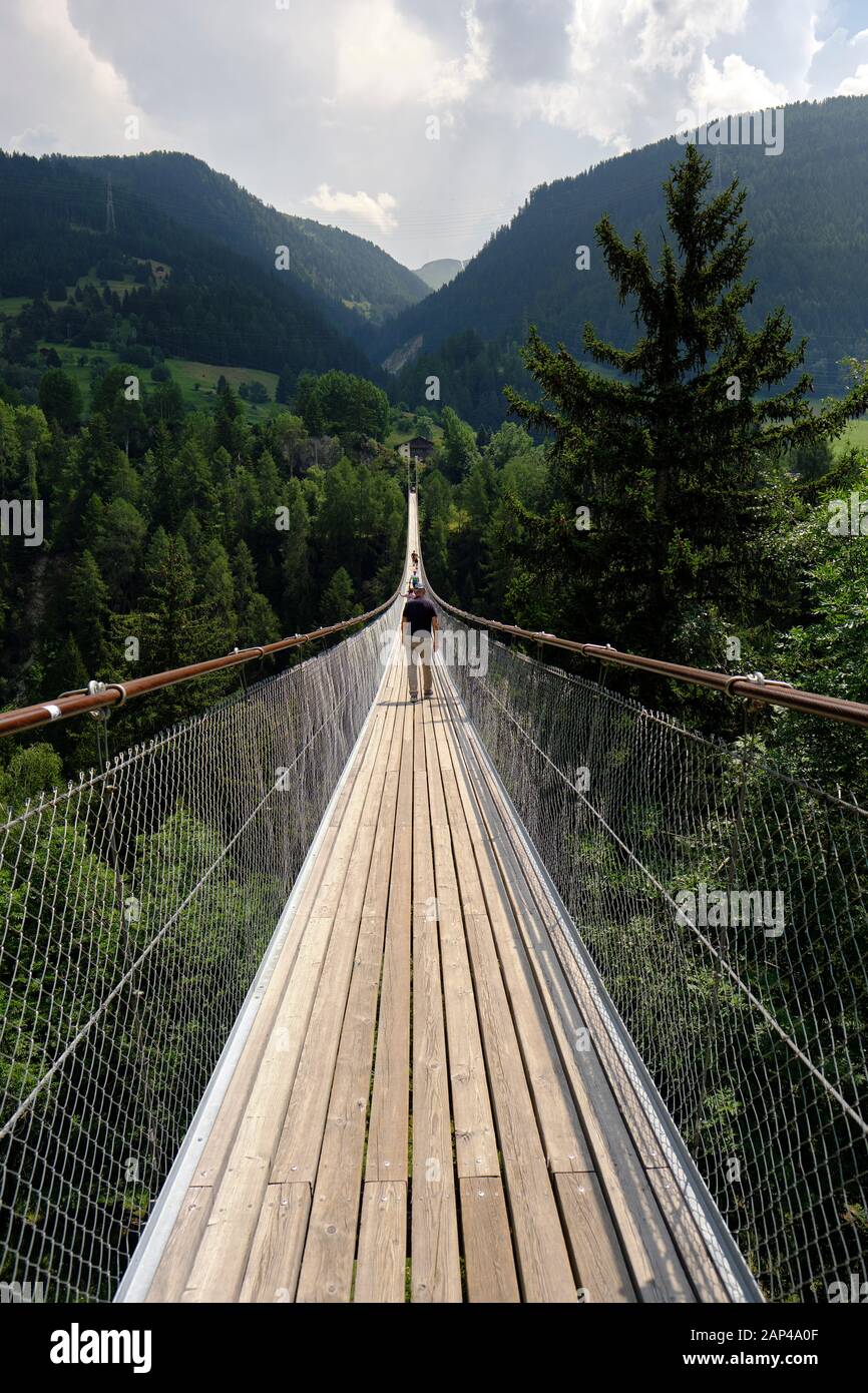 A hiker crossing Goms Bridge one of the longest suspension footbridges in Valais in the Swiss Alps connecting the villages of Fürgangen and Mühlebach. Stock Photo