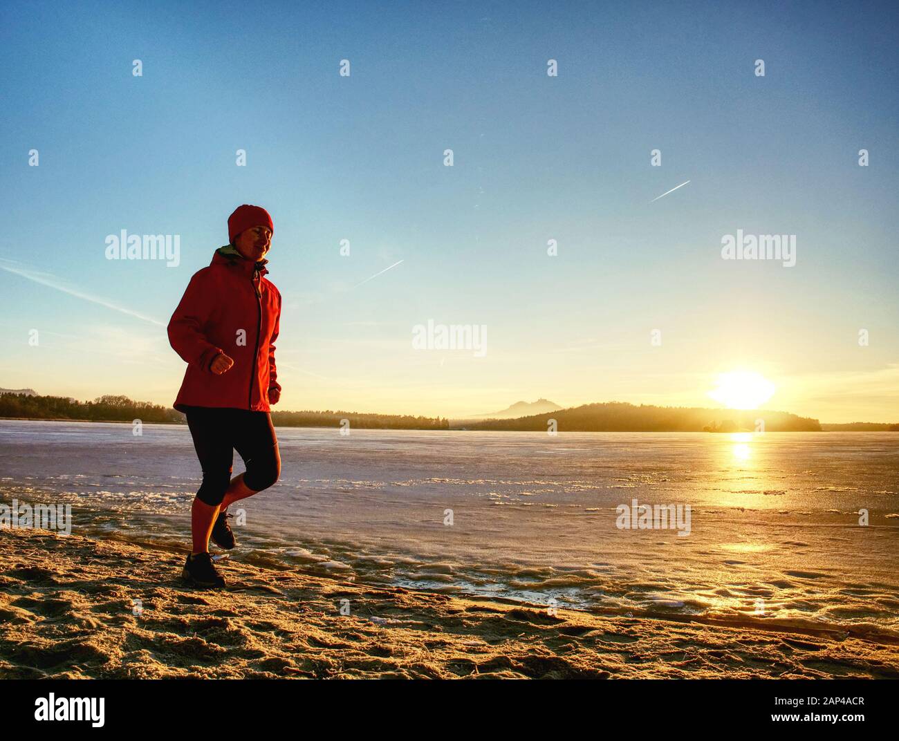Woman or girl running in winter river park by evening. Happy face of running woman within