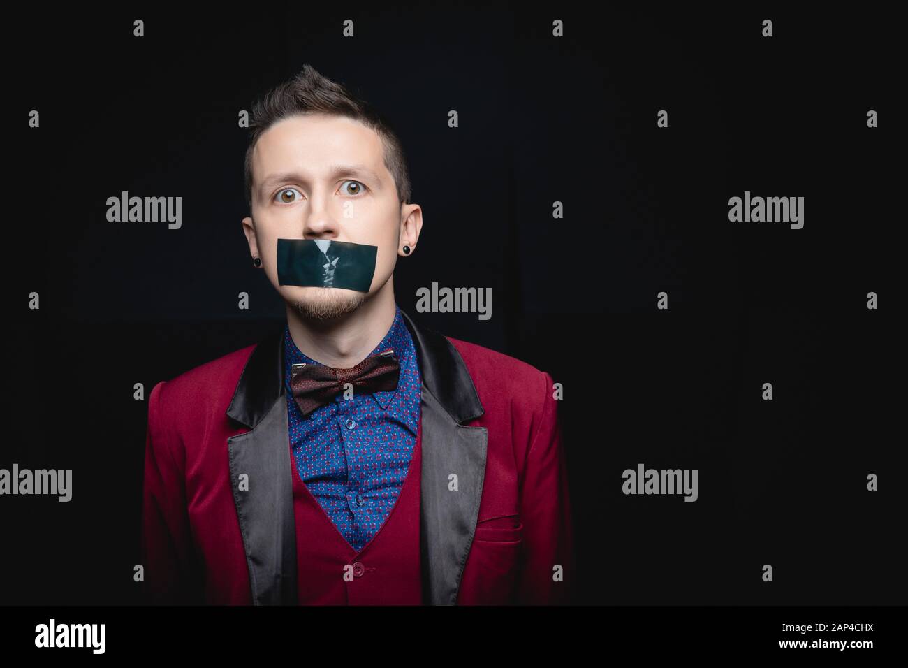 Man in red jacket with closed tape over his mouth. Black isolated background Stock Photo