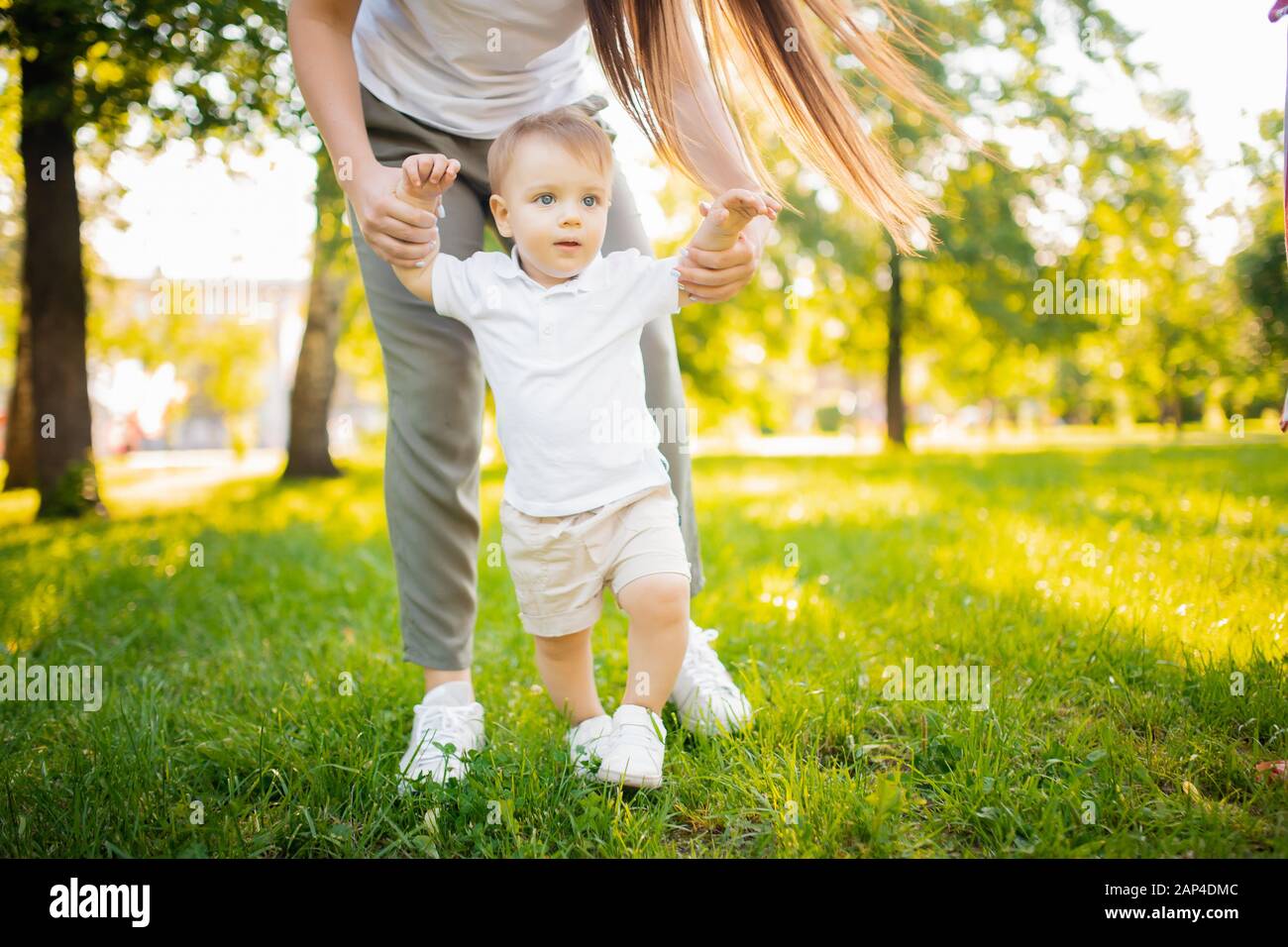 Child baby takes first step with help of mom in park. Concept parents teach walking Stock Photo