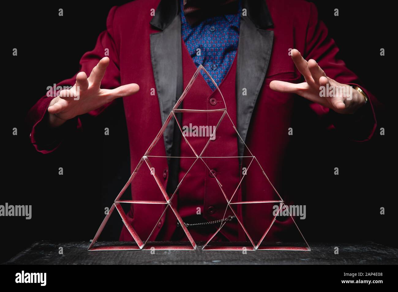 Magician shows trick pyramid with playing cards on dark background Stock Photo