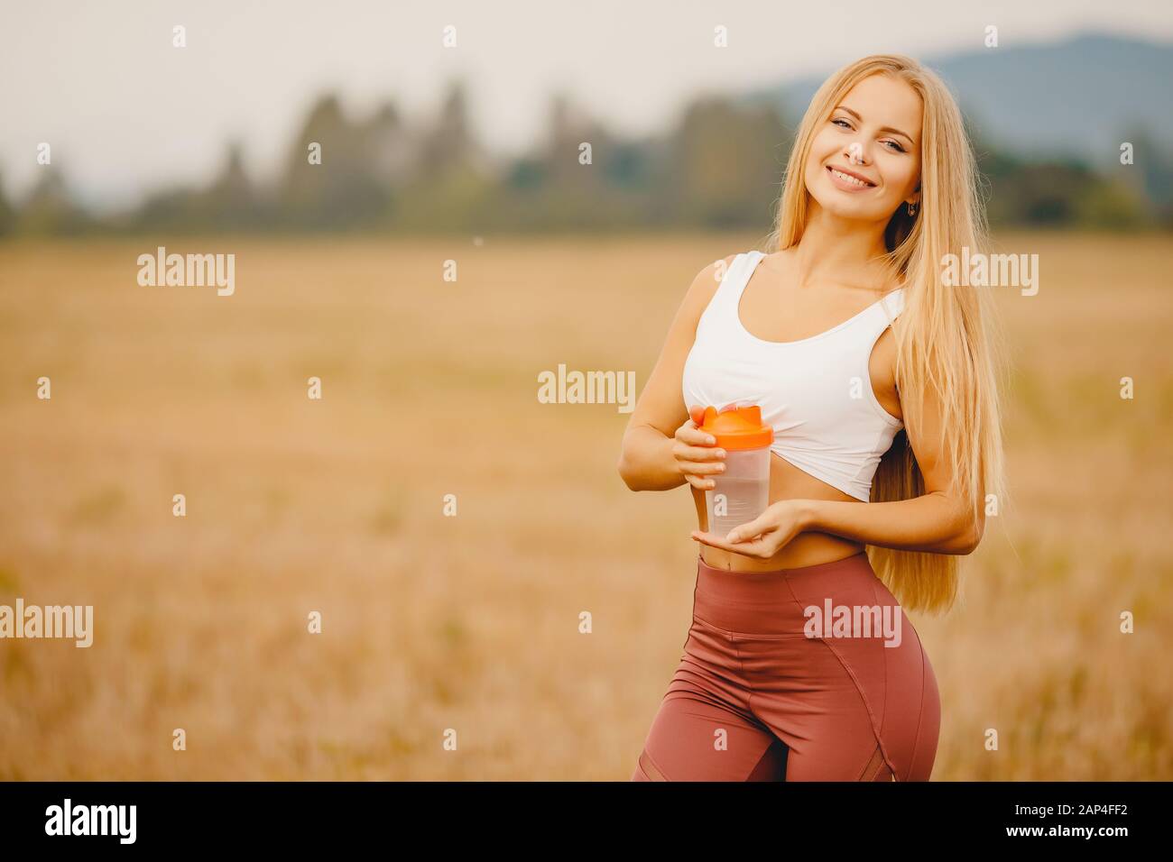 Download Beautiful Blonde Girl Holding Shaker Bottle Of Water On Park Background Looking Camera And Smiling Stock Photo Alamy PSD Mockup Templates