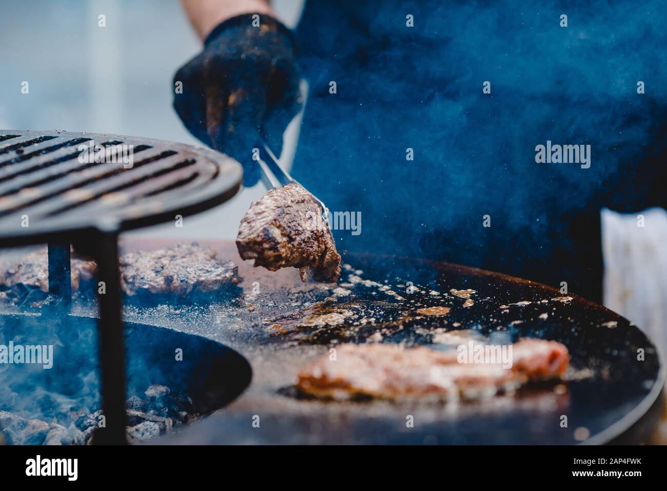 Cook grills steaks and pork ribs open fire. Turns meat over with tongs