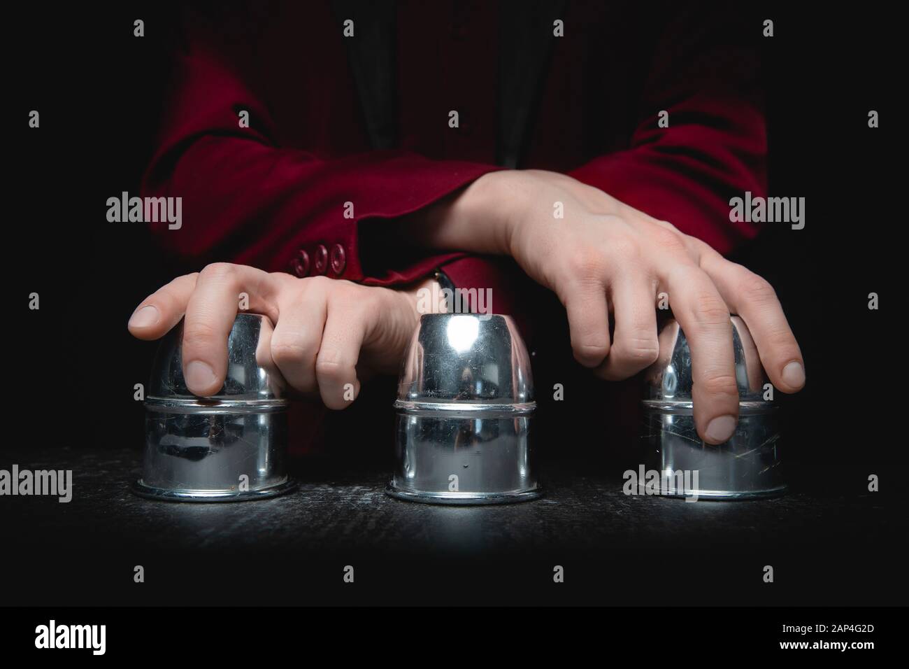 Magician shows shell game of thimbles with circles and ball, black background. Concept deception, sleight hand Stock Photo