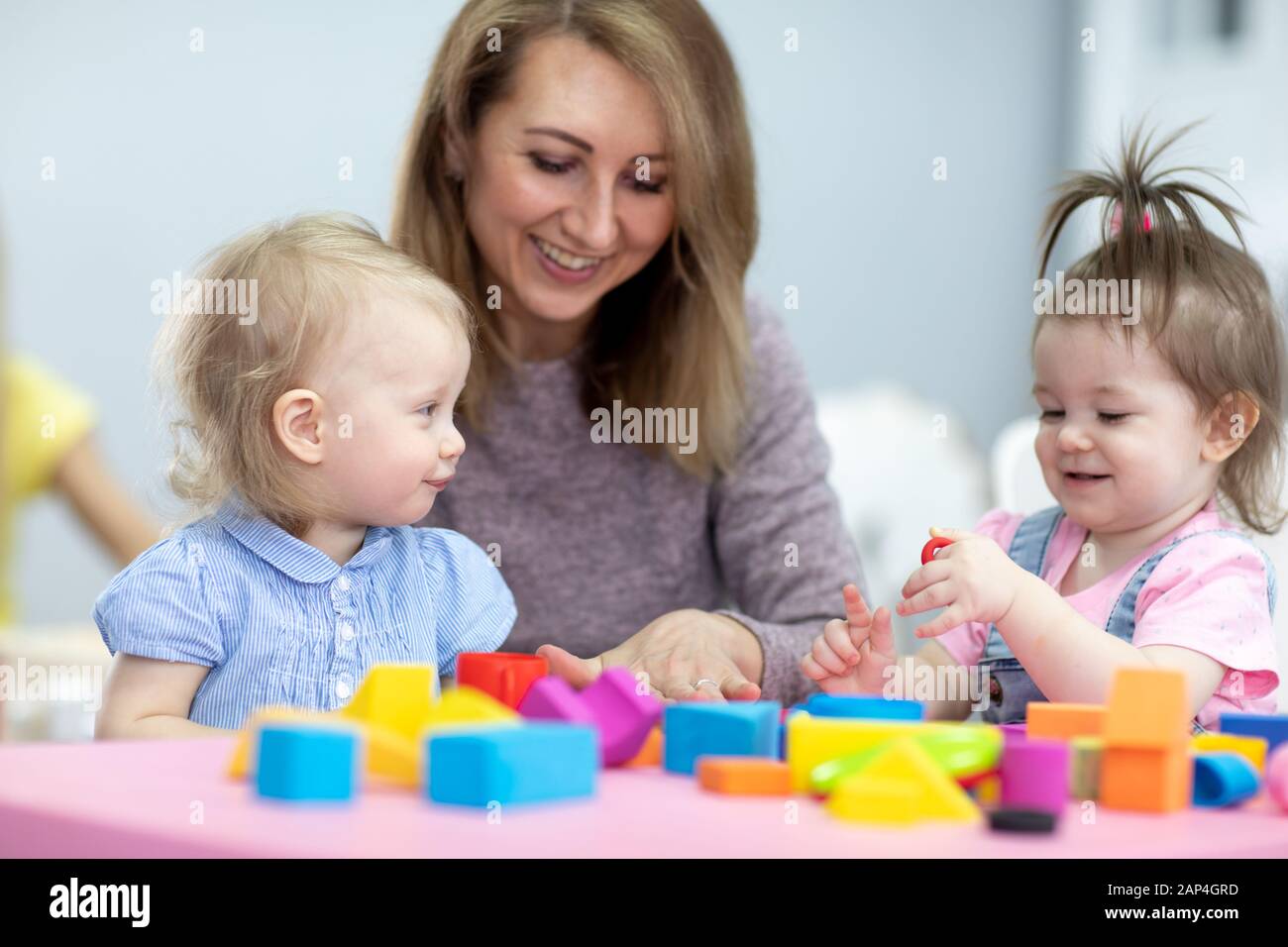 children toddlers playing with teacher in nursery or daycare Stock Photo