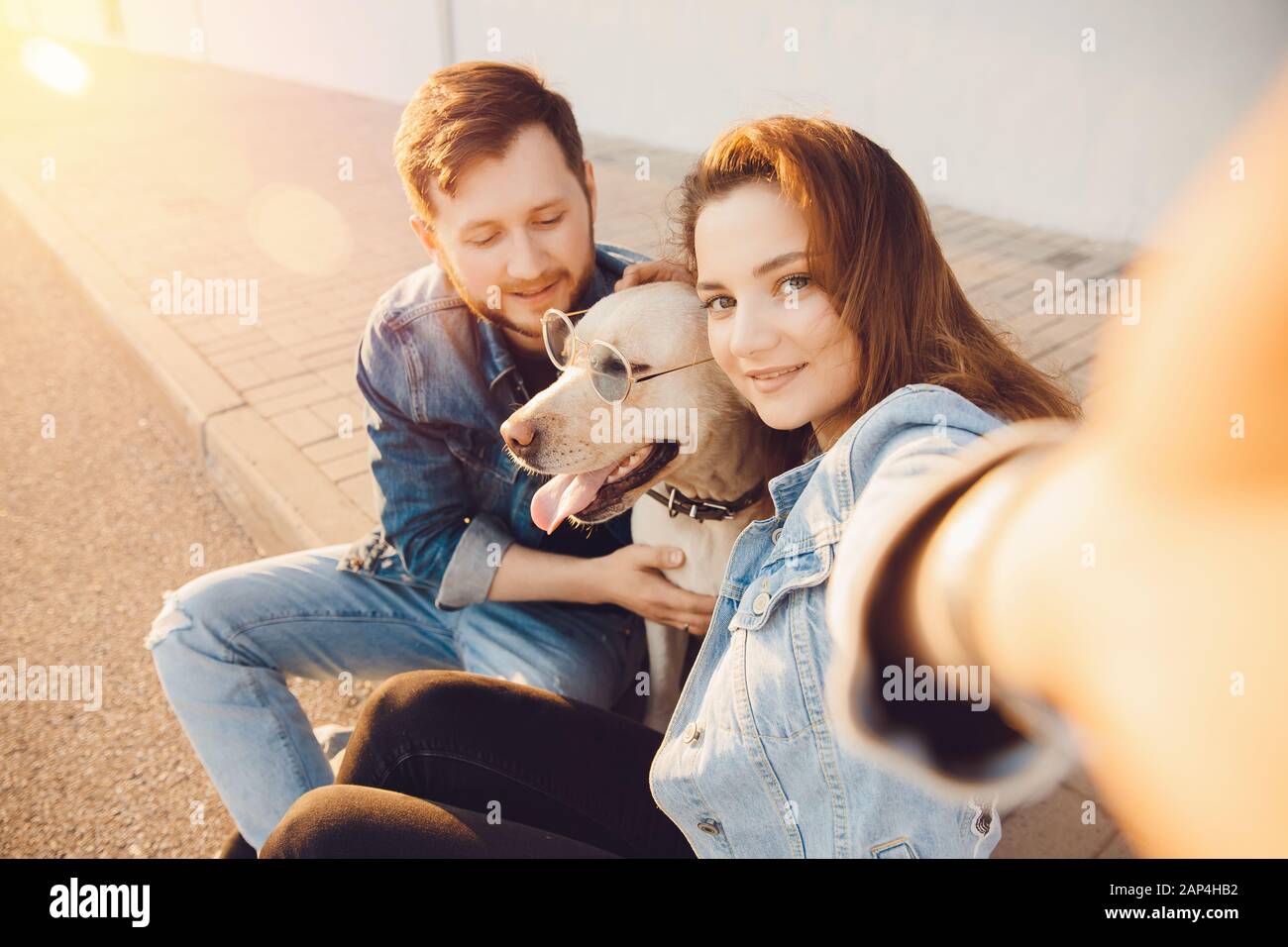 Happy beautiful couple is having fun with labrador dog retriever outdoors making selfie photo Stock Photo