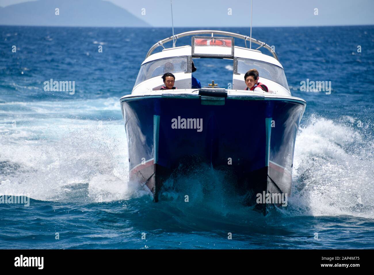 Two Boys having fun travelling at high speed on a boat in sun on blue ocean and sea spray wash Stock Photo
