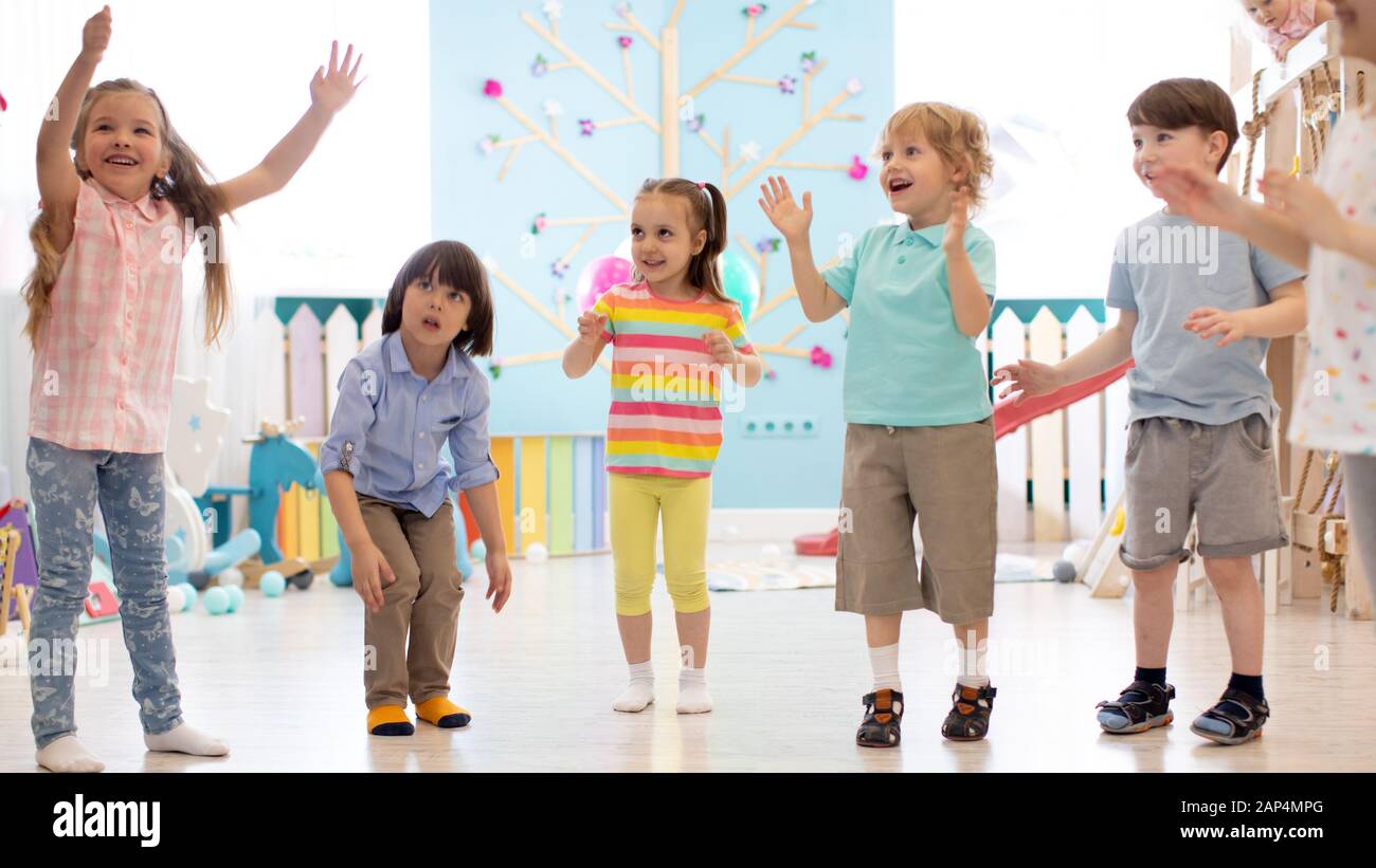Cheerful kids stand semicircle on floor in kindergarten or daycare centre. Preschoolers have fun indoors, playing games Stock Photo
