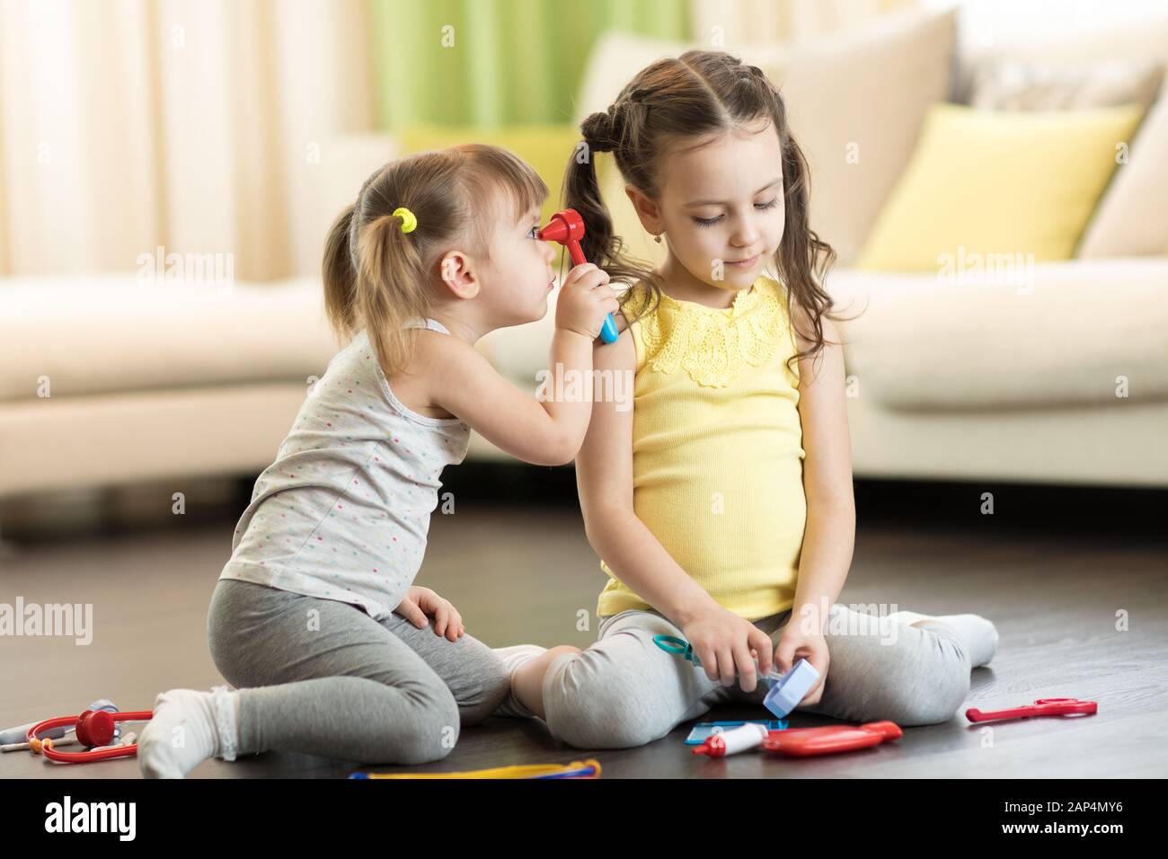 Funny kids playing doctor with toy tools. Children sitting on floor in living room Stock Photo