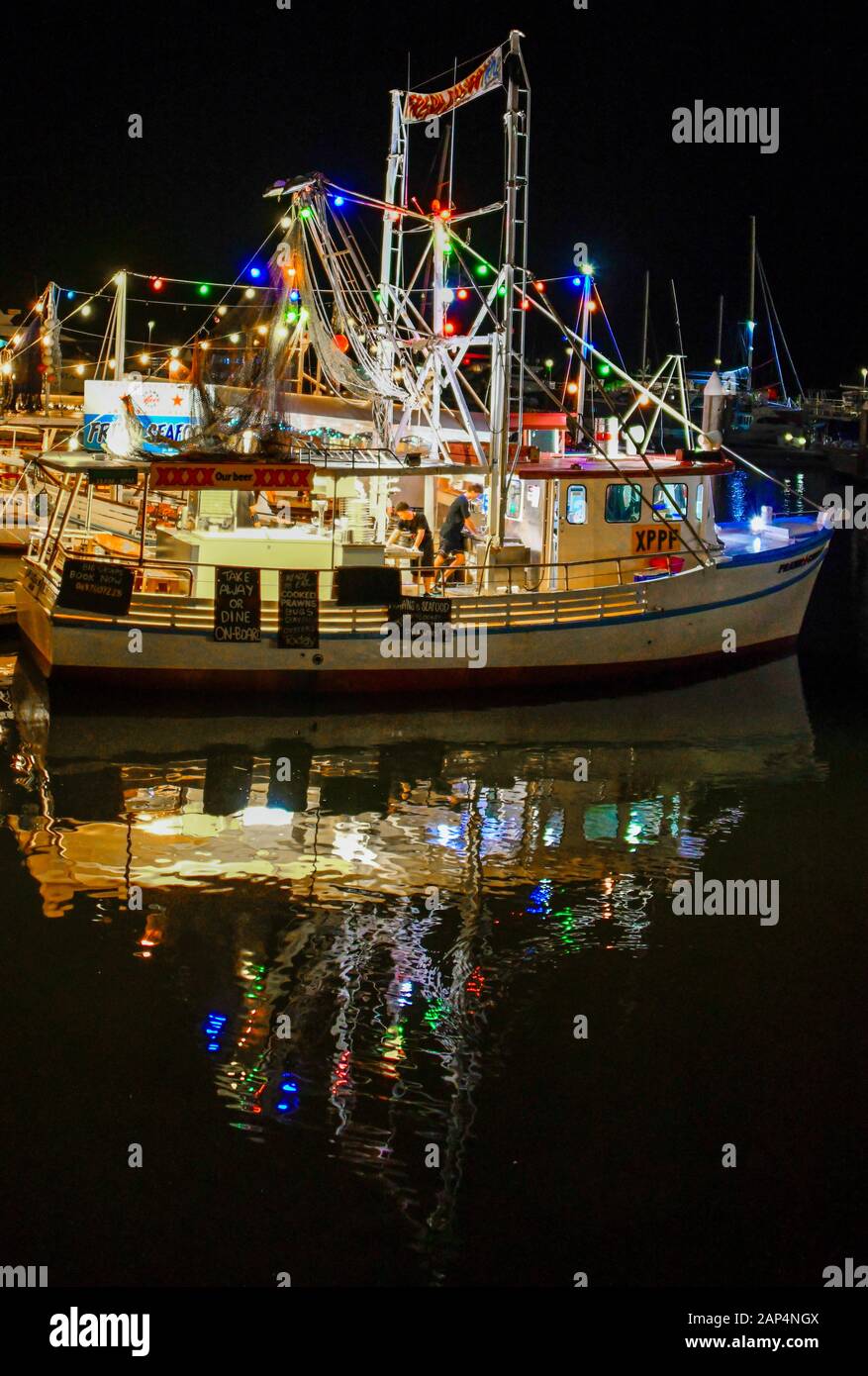 Prawn Star floating seafood restaurant trawler boat, fresh seafood offerings at night with colourful reflections, Cairns Marina, Queensland, Australia Stock Photo