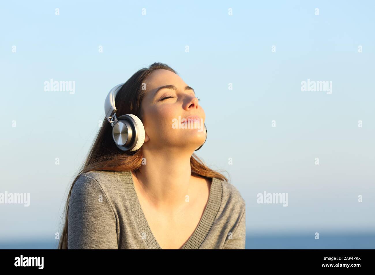 Relaxed woman wearing headphones meditating listening to music on the beach at sunset Stock Photo