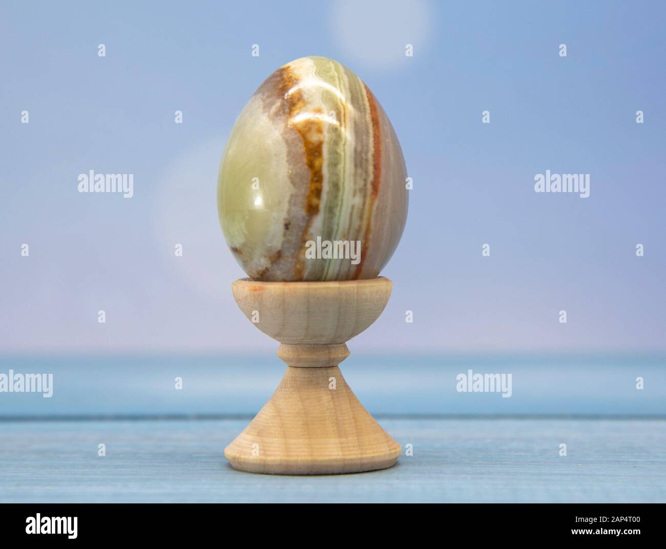 One multi-colored stone egg on a wooden stand on a blurred background ...