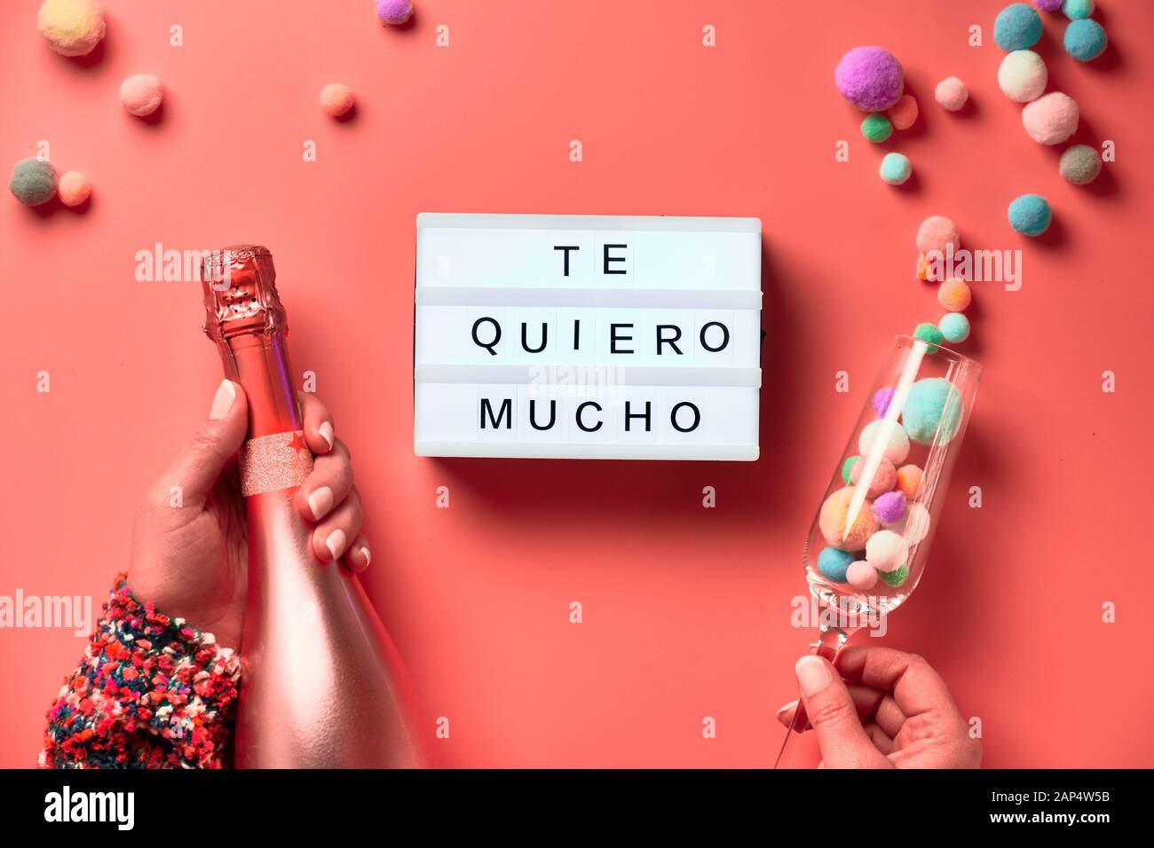 Text 'Te quero mucho' means I love you so much in English. Lightboard with text in Latino female hands, flat lay on pink background. Bottle of champag Stock Photo