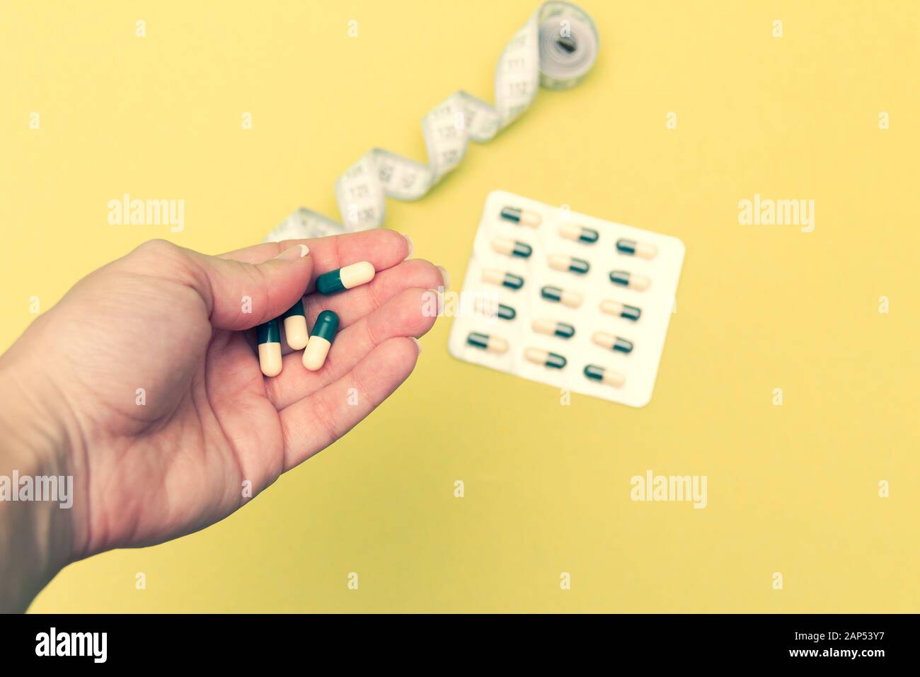 Diet pills in woman's hand and measuring meter on yellow background. Losing weight concept. Stock Photo
