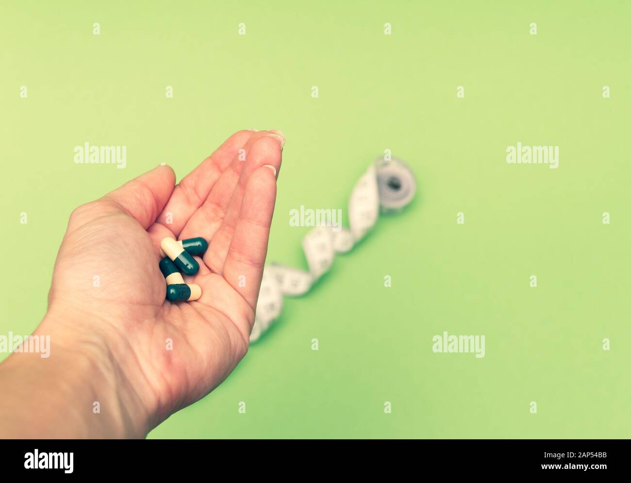 Diet pills in woman's hand and measuring meter on green background. Losing weight concept. Stock Photo