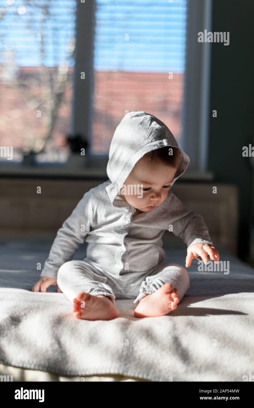 Happy baby boy in grey pyjamas on bed in his room. Sunny day in sweet house Stock Photo