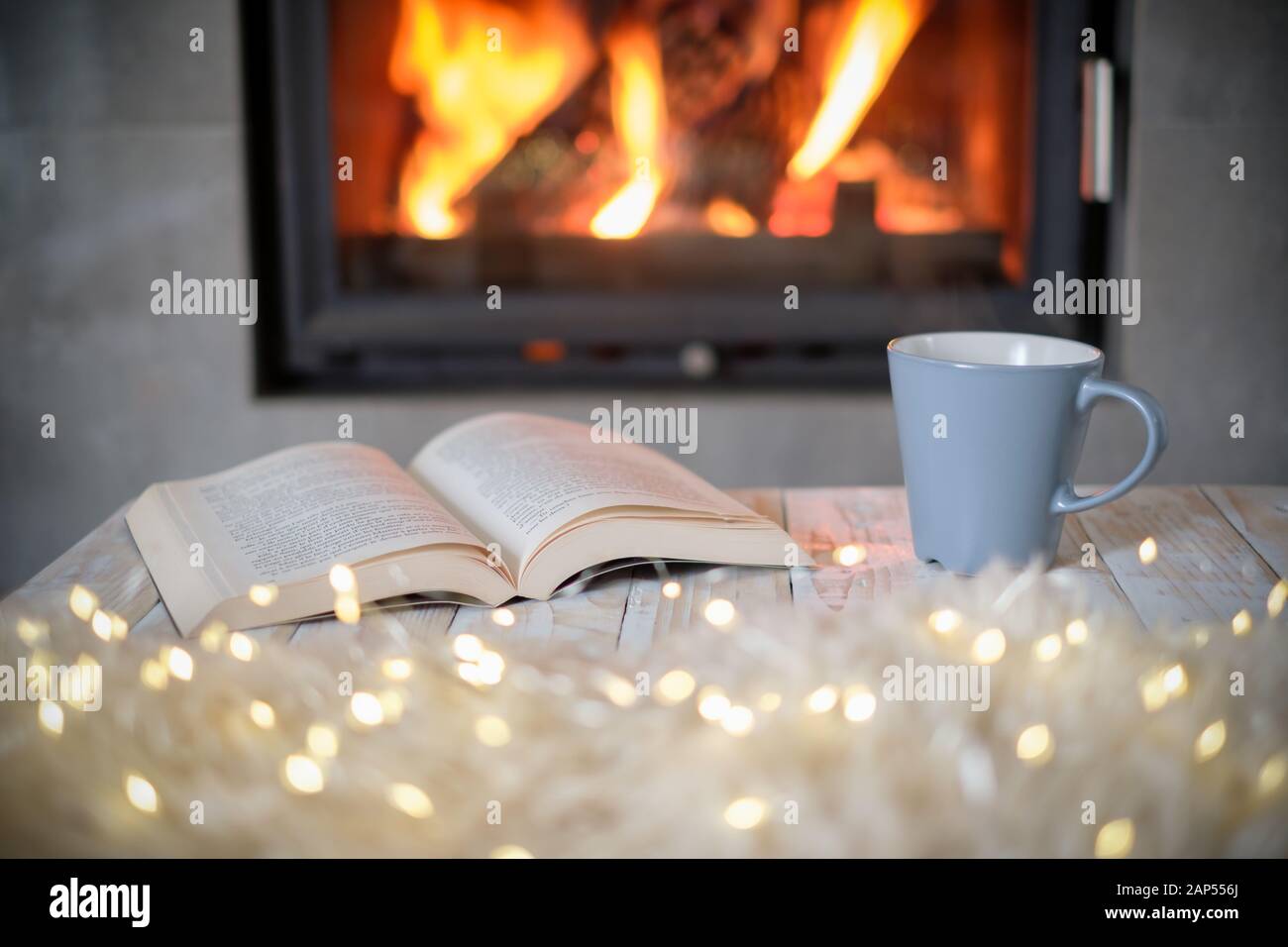 Open book and cup of tea near burning fireplace. Hygge concept Stock Photo