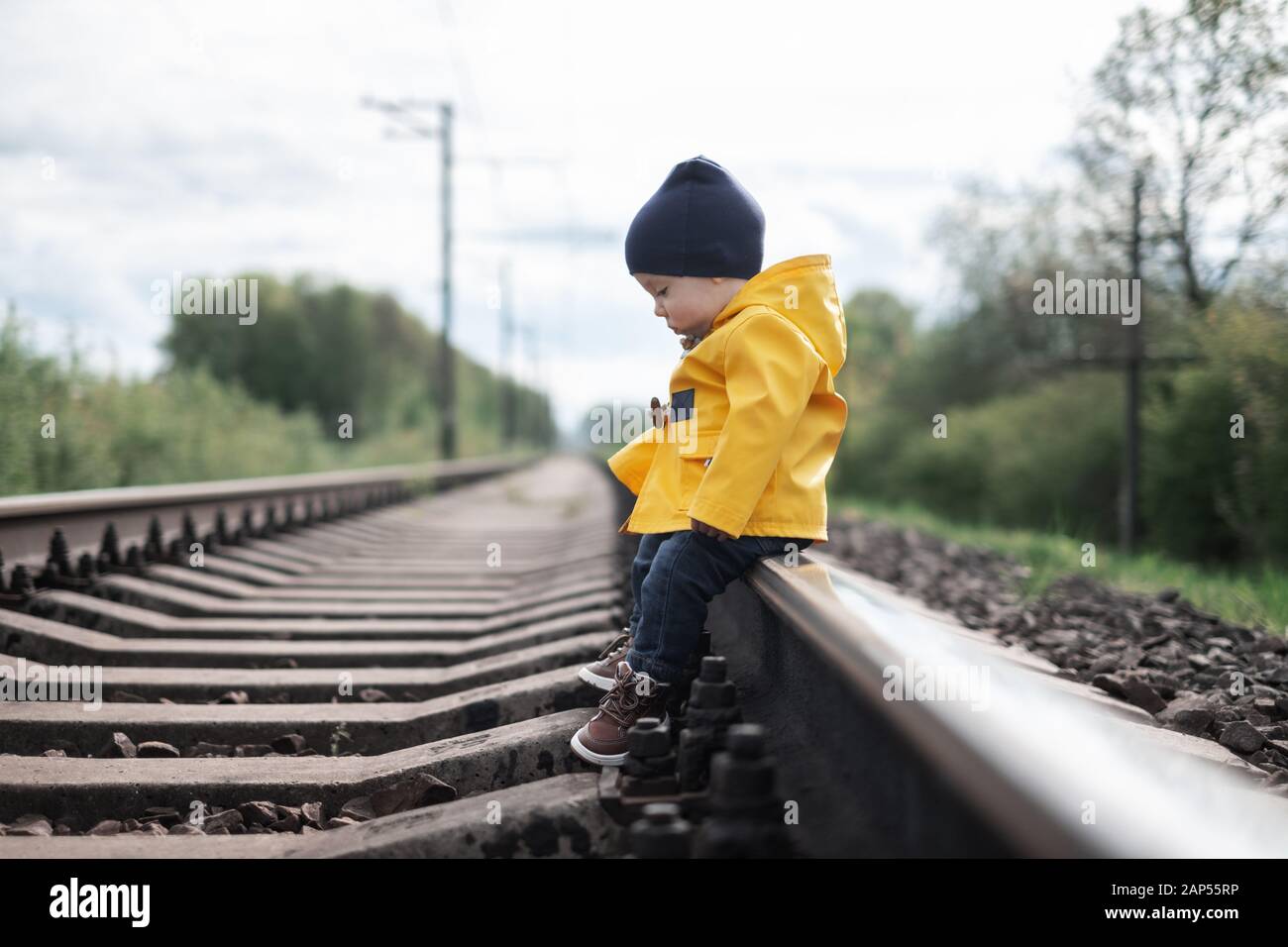 Kid in yellow jacket sitting on railroad Stock Photo