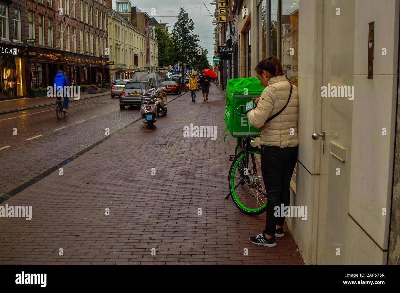 Amsterdam, Holland, August 2019. A rainy day in the shopping street. An uber eat worker consults the smartphone, next to the bike with the showy green Stock Photo