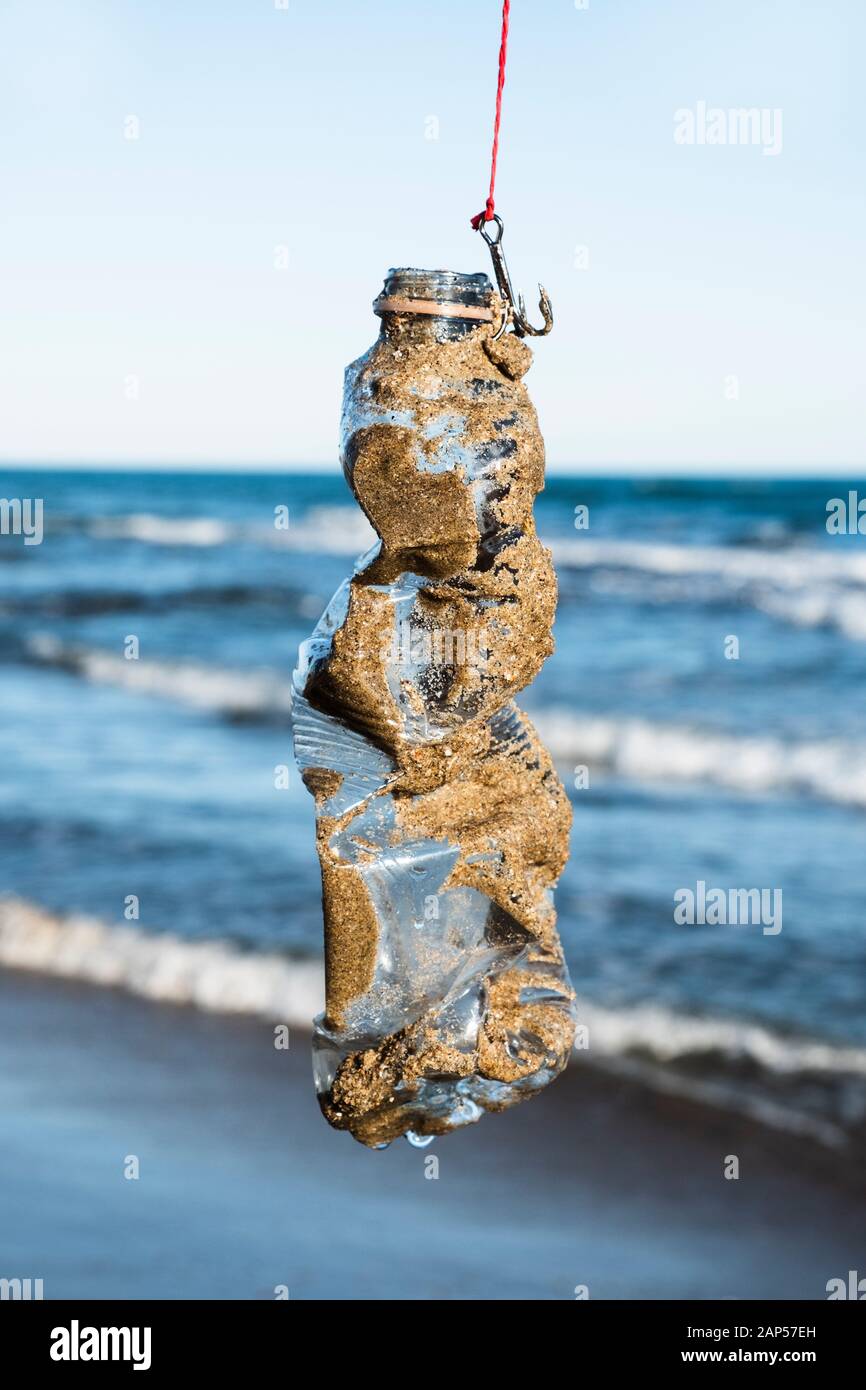 closeup of a used plastic bottle, covered with wet sand, in a fish hook, freshly fished in the ocean Stock Photo