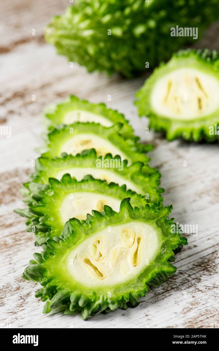 closeup of some slices of raw karela, also known as bitter melon or bitter gourd, on a white rustic wooden table Stock Photo
