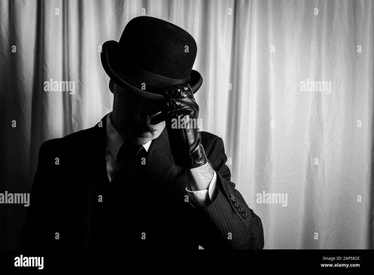 Portrait of Man in Dark Suit and Leather Gloves Doffing Bowler Hat. Concept of Classic and Eccentric British Gentleman. Retro Fashion. Stock Photo