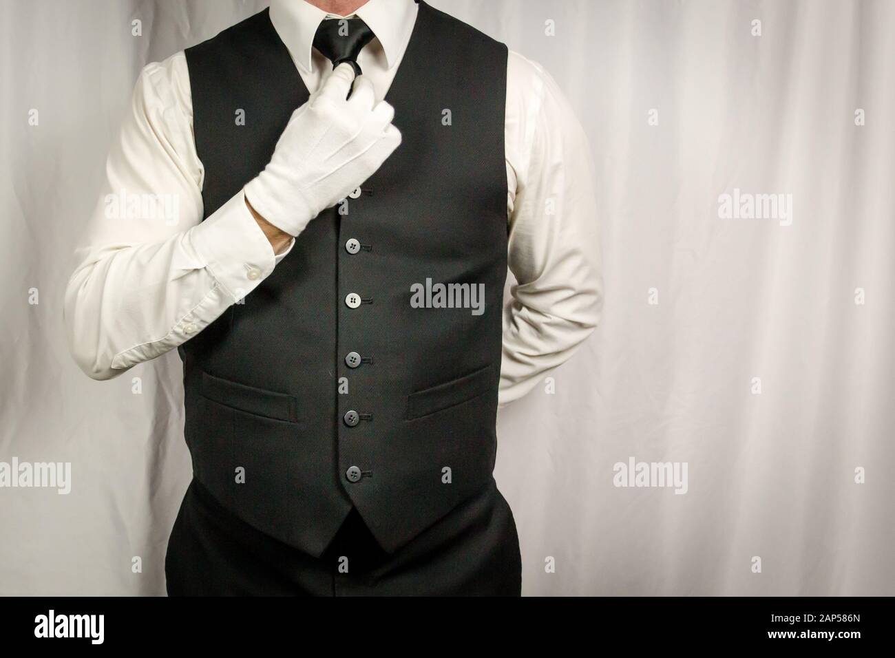 Man in Waistcoat and White Gloves Straightening Tie. Concept of Service Industry and Professional Hospitality and Courtesy. Stock Photo